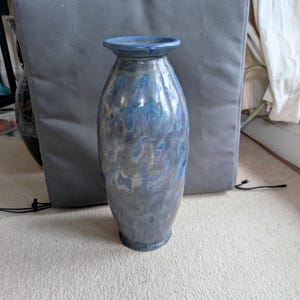 May include: A tall, ceramic vase with a flared rim and a rounded base. The vase has a glossy, iridescent finish in shades of blue, gray, and silver. The vase is approximately 12 inches tall.