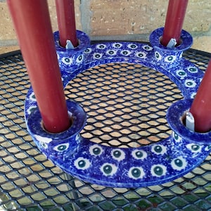 May include: Blue and white ceramic candle holder with four candle slots. The holder is decorated with a pattern of blue eyes and green accents.