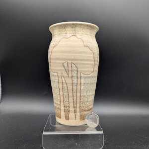 Op de afbeelding: Een beige keramische vaas met een boomontwerp. De vaas heeft een cilindrische vorm met een licht uitlopende rand. Het boomontwerp is in een donkerdere bruine kleur en de vaas is ongeveer 15 cm hoog.