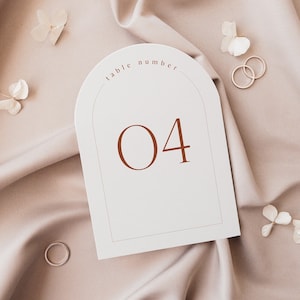May include: White table number card with a rounded arch at the top. The card says "table number" and "04" in brown text.