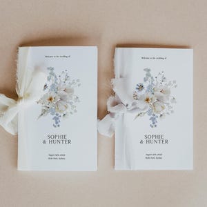 May include: Two wedding programs with floral designs and ribbon ties. The programs are white with a watercolor floral arrangement in shades of white, blue, and green. The text reads "SOPHIE & HUNTER" and event details.