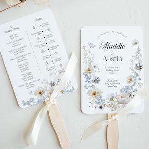 Puede incluir: Dos abanicos de boda blancos con diseños florales azules. El abanico de la izquierda tiene un horario de la ceremonia de boda y el abanico de la derecha dice "Bienvenido a la boda de Maddie & Austin".