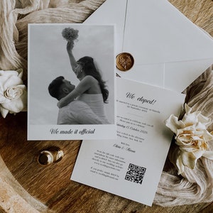 May include: A black and white photograph of a couple holding a bouquet of flowers. The photo is framed with a white border and the text "We made it official" is printed below the photo. The photo is on a white card with the text "We eloped!" and information about their wedding.