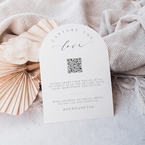 Puede incluir: Tarjeta blanca con un código QR en blanco y negro, el texto "Capture the love" en letra cursiva, y el texto "¡Comparte tus fotos con nosotros! Simplemente escanea el código QR con tu teléfono inteligente y súbelo. Cuando compartas en las redes sociales, usa nuestro hashtag #OURHASHTAG".