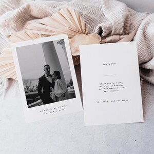 Può includere: Una foto di matrimonio in bianco e nero di una coppia in piedi davanti a una colonna. La foto è su un cartoncino bianco con il testo "Sophia & James 26 aprile 20xx" stampato sotto la foto. Il cartoncino è accanto a un cartoncino bianco con il testo "Grazie! Grazie per essere stati lì al nostro matrimonio. Avete reso la giornata ancora più speciale. I nuovi sig. e sig.ra Stone" stampato su di esso.