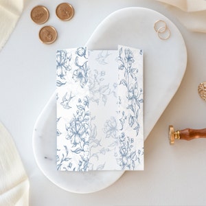 May include: A folded white card with a blue floral pattern and small birds. The card is on a white marble surface.