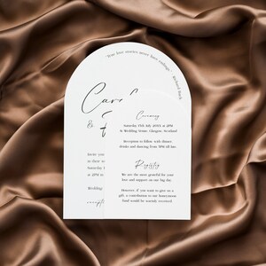 May include: A white wedding invitation with a modern arch design. The invitation features the couple's names, "Carr & t", the wedding date, "Saturday 15th July 20XX at 2PM", and the wedding venue, "At Wedding Venue, Glasgow, Scotland". The invitation also includes details about the reception, which will follow with dinner, drinks, and dancing from 5PM till late.