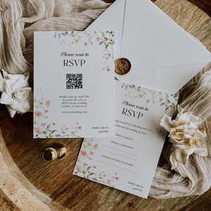 May include: Wedding RSVP cards with floral accents and the text "Please scan to RSVP." The cards include a QR code and a space for guest information. An envelope with a wax seal and a white flower are also present.