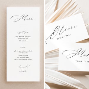 May include: Elegant white wedding stationery set. Includes a menu card with a cursive "Menu" heading and a detailed list of courses. Also features place cards with names and table numbers in a matching script.
