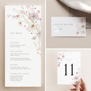 Può includere: Set di partecipazioni di nozze con disegni floreali ad acquerello. Il set include un menu, un segnaposto e un numero di tavolo. Il menu elenca antipasti, piatti principali e dessert. Il segnaposto recita "Evelyn Winter, table eight." Il numero del tavolo è "11."