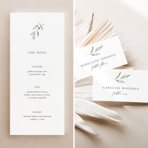 May include: A wedding menu with a simple design featuring a sprig of greenery. The menu lists starters, main course, and dessert. Two place cards with a similar design are shown with the names "Madeleine Johnson, Table Three" and "Caroline Roseman, Table One".