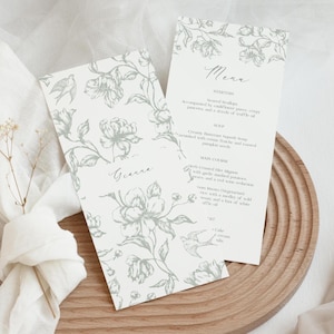 May include: Two wedding menu cards with floral and bird illustrations in gray. One card has the name "Gianna" and the other has a menu with starters, soup, and main course options. The cards are on a wooden tray.