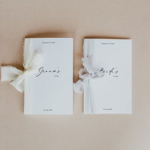 May include: Two white paper booklets with the words "Groom's Vows" and "Bride's Vows" printed on them. Each booklet is tied with a white ribbon.