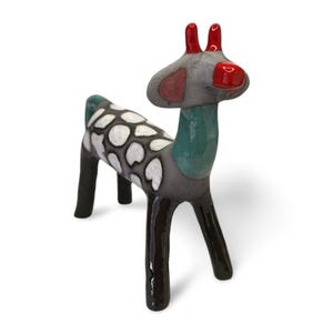 May include: A ceramic deer figurine with a gray body, black legs, and a green neck. The deer has white spots on its back, red accents on its ears and nose, and stands on a white surface.