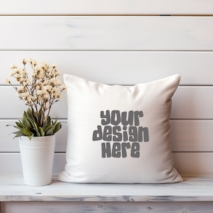 Op de afbeelding: Een wit kussen met de tekst "your design here" in grijze letters op een witte houten achtergrond.