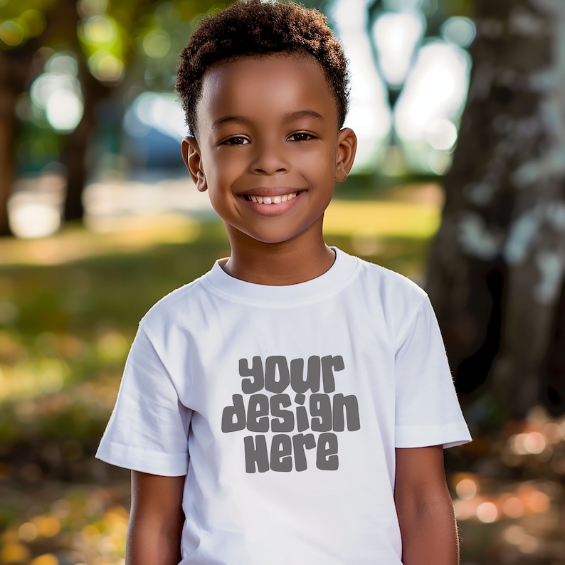 May include: A young boy wearing a white t-shirt with the text "your design here" printed on the front. He is smiling and looking at the camera.
