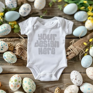 May include: A white baby onesie with the text "your design here" in grey on a wooden background surrounded by colourful Easter eggs.