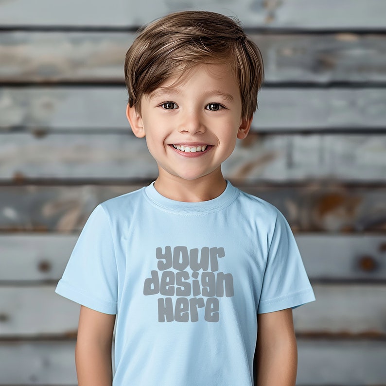 May include: A young boy wearing a light blue t-shirt with the text "your design here" in gray. The boy is smiling and looking at the camera.