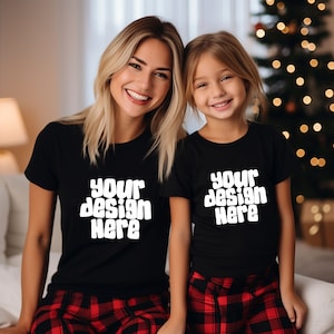 May include: Two people wearing black t-shirts with the text "Your design here" in white. The shirts are a matching set. The people are wearing red and black plaid pajama pants.