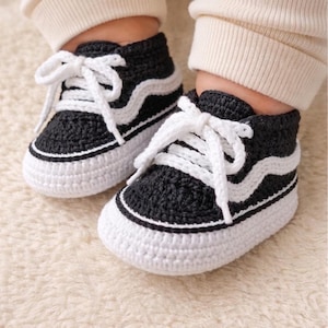 May include: A pair of black and white crochet baby sneakers. The shoes have white soles, laces, and a wave design. The miniature shoes are designed to resemble classic trainers.
