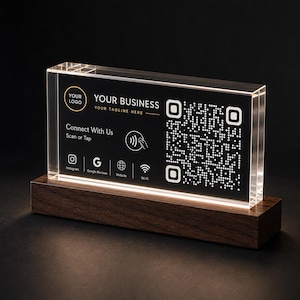 Può includere: Un cartello rettangolare in acrilico trasparente con un inserto nero che presenta un codice QR, il testo YOUR BUSINESS, YOUR TAGLINE HERE, Connect With Us, Scan or Tap, e icone per Instagram, Google Reviews, Website e Wi-Fi, su base in legno.