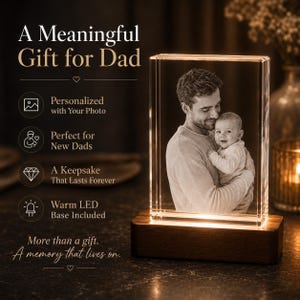 May include: A rectangular glass block featuring a laser-etched black and white photograph of an adult holding a baby. The glass sits on a dark brown wooden base that emits a warm LED light. Text on the left reads A Meaningful Gift for Dad.
