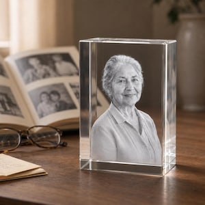 May include: A rectangular clear glass block featuring a three-dimensional laser-etched portrait of an older person with short hair, wearing a collared shirt. The image is rendered in monochrome tones within the solid, transparent glass structure.