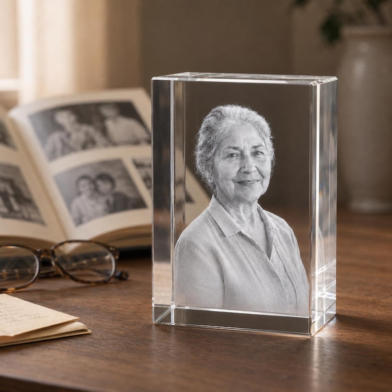 May include: A rectangular clear glass block featuring a three-dimensional laser-etched portrait of an older person with short hair, wearing a collared shirt. The image is rendered in monochrome tones within the solid, transparent glass structure.