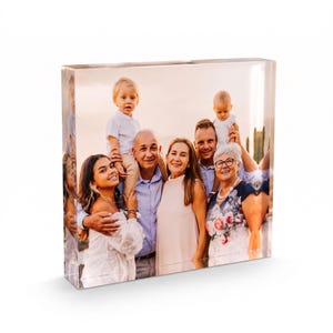 May include: A rectangular clear acrylic photo block featuring a printed family portrait. The image displays a multi-generational group including a young child, a baby, and several adults, all captured in a warm, outdoor setting with soft lighting.