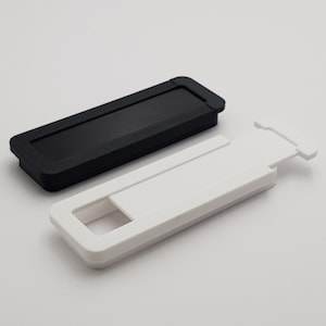 May include: Two webcam covers, one black and one white. Both covers are rectangular and have a small rectangular opening in the centre. The covers are designed to slide over the webcam lens to protect privacy.