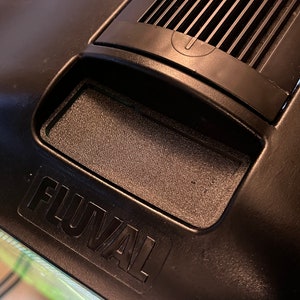 May include: A black Fluval aquarium filter with a rectangular opening and a black plastic cover. The filter has a black power button and a black vent.