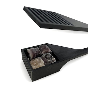 Könnte beinhalten: Ein schwarzer Plastikspender mit einem Klappdeckel, der kleine, quadratische Bonbons in verschiedenen Farben enthält. Der Spender hat einen Griff zum einfachen Tragen.