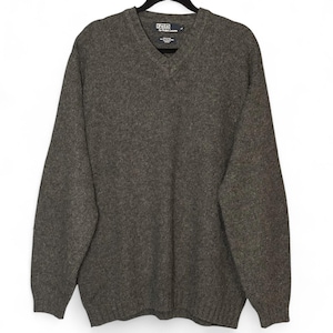 Puede incluir: Un suéter gris oscuro con cuello en V y mangas largas, colgado de una percha negra. El suéter tiene una textura acanalada y una etiqueta con la marca "Polo by Ralph Lauren".