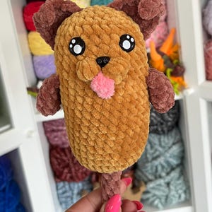 Peut inclure: Un jouet pour chien en peluche fait à la main, dans les tons marron et beige. Le chien a de grands yeux expressifs, une langue rose et des oreilles et des pattes marron. Le jouet est fait de fil doux et texturé et est conçu pour ressembler à un chien de dessin animé.