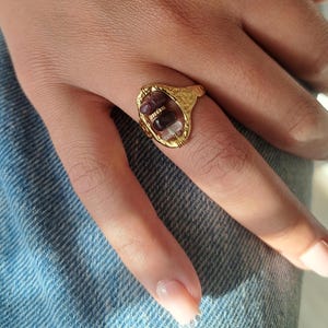 May include: Gold ring with a textured oval setting featuring three different coloured stones. The stones are a dark red, black, and white.