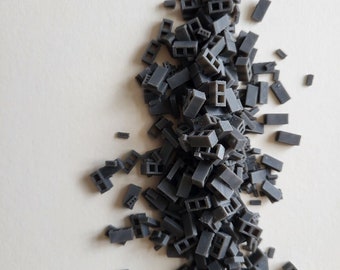 Könnte beinhalten: Ein Haufen kleiner, grauer Miniatur-Ziegelsteine, die auf einer weißen Oberfläche verstreut sind. Die Steine haben eine rechteckige Form mit zwei hohlen Öffnungen. Das Bild zeigt die Steine in einer zufälligen Anordnung.