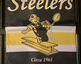 May include: Black and yellow Pittsburgh Steelers flag with a cartoon worker kicking a football. The flag says "Pittsburgh Steelers" and "Circa 1961 Established 1933".