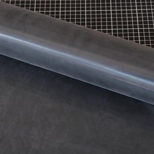 May include: A roll of dark gray leather material, partially unrolled, revealing a smooth surface. The leather is a solid color with subtle variations in tone. The background features a black and white grid pattern.
