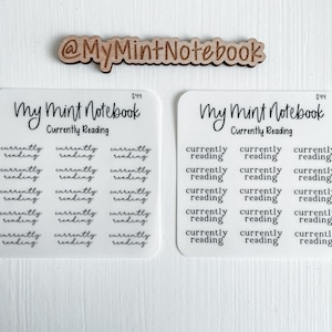 Puede incluir: Una hoja de pegatinas transparentes con el texto "Currently Reading" y la frase "My Mint Notebook" repetida varias veces. Las pegatinas están diseñadas para usar en un planificador o diario.