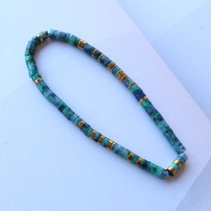 Puede incluir: Un collar de piedras preciosas azules y verdes con detalles dorados. El collar está hecho de pequeñas cuentas cuadradas.