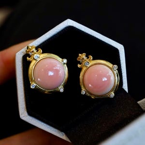 Può includere: Un paio di orecchini d'oro con cabochon di corallo rosa e dettagli in diamanti. Gli orecchini hanno un design a forma di corona.