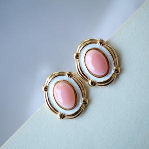 Può includere: Un paio di orecchini dorati con smalto bianco e pietre ovali rosa.