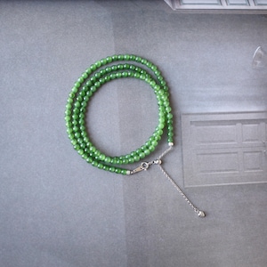May include: A green jade bead necklace with a silver adjustable clasp. The necklace is made of small, round beads and is layered for a delicate look.
