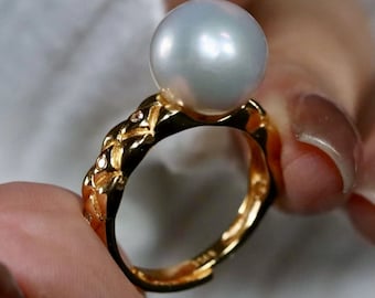 May include: A gold ring with a large white pearl and a detailed, textured band.