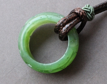 May include: A green jade ring pendant with a brown leather cord. The ring is smooth and has a speckled texture.