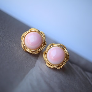 Può includere: Un paio di orecchini d'oro con cabochon di conchiglia rosa. Gli orecchini hanno un design delicato e intricato.