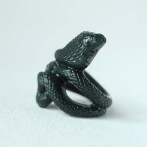 Peut inclure: Une bague serpent vert foncé. La bague présente un motif de serpent détaillé, le corps du serpent s'enroulant autour du doigt. La tête du serpent est relevée et les écailles sont visibles. La bague est en matériau solide.