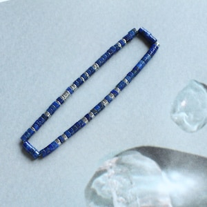 Op de afbeelding: Een blauwe lapis lazuli kralenketting met zilveren accenten. De ketting is gemaakt van kleine, vierkante kralen.