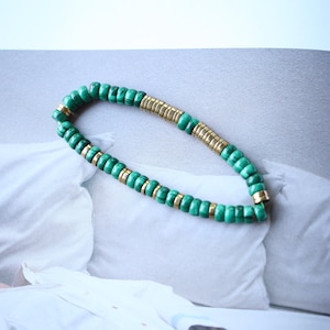 Op de afbeelding: Een groene en gouden kralen armband met een eenvoudig ontwerp. De armband is gemaakt van kleine, ronde kralen die aan elkaar geregen zijn op een dun koord.