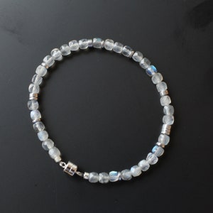 Pode incluir: Uma pulseira delicada com contas facetadas e translúcidas com tons sutis de azul e branco. As contas são intercaladas com pequenos detalhes metálicos prateados. A pulseira é montada em um cordão flexível e possui um fecho magnético.